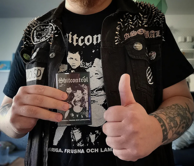 A closeup photo of me holding their tape, wearing their shirt, giving a thumbs up